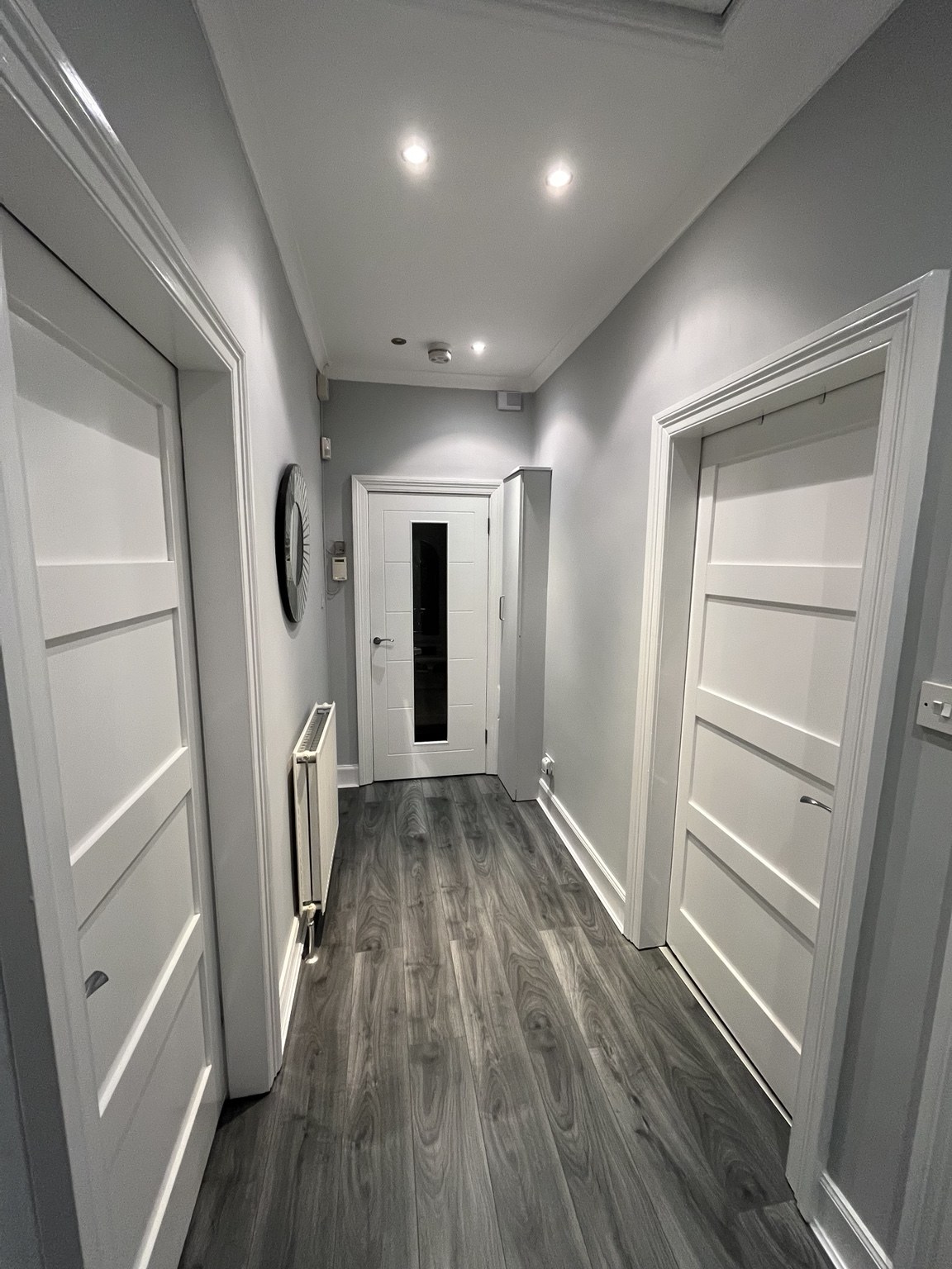Hallway with white internal doors, recessed lighting and grey timber-effect flooring