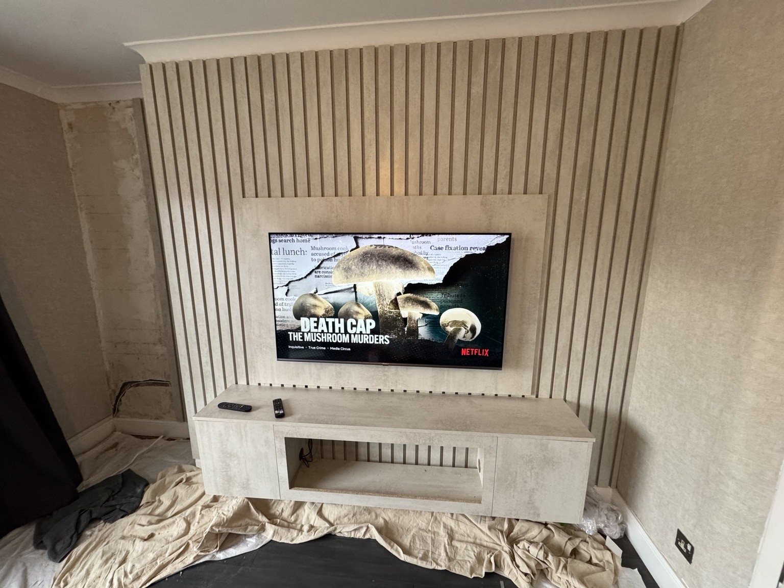 Media wall during installation, showing full-height slatted panels, mounted television and floating storage unit before the fireplace is fitted