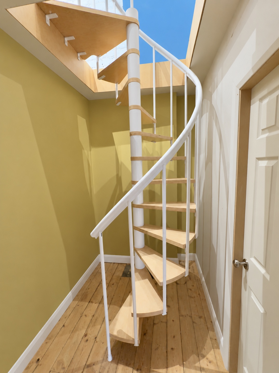 Spiral staircase with timber treads and a white handrail beneath a ceiling opening
